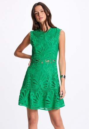 Abito verde in pizzo con un motivo a farfalla, bordi scallop e gonna a ruota. Design senza maniche con dettagli a taglio.