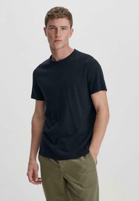 Donkerblauwe katoenen t-shirt met korte mouwen, ronde hals en een relaxte pasvorm, gecombineerd met lichtgekleurde broeken. Soepele textuur en eenvoudig ontwerp.