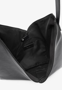 Borsa a spalla nera in pelle aperta per mostrare l'interno rivestito in tessuto liscio e una piccola tasca interna con chiusura a scatto.