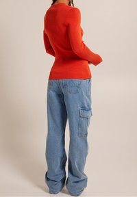 Pull en orange côtelé à manches longues associé à un jean cargo baggy bleu clair avec poches latérales et une coupe décontractée.