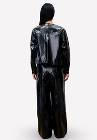 Veste noire en cuir courte et pantalon large, présentant une texture lisse et un design minimaliste, vue de dos.