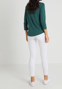 Teal katoenen top met driekwartmouwen, gecombineerd met witte skinny jeans. De outfit bevat witte sneakers en heeft een eenvoudig ontwerp.
