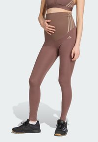 Leggings de maternité en tissu extensible marron ; design taille haute avec un panneau de soutien, associés à des chaussures de sport noires.