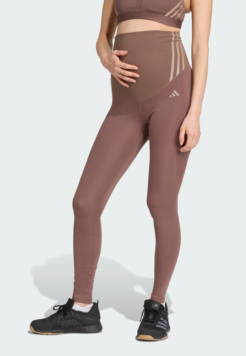 Leggings de maternité en tissu extensible marron ; design taille haute avec un panneau de soutien, associés à des chaussures de sport noires.