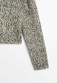 Manche longue d'un pull en maille épaisse avec un motif chiné noir et blanc sur fond blanc.