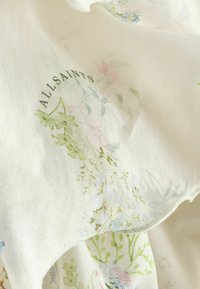Blødt hvidt stof med delikate pastelfarvede blomsterprint og ordet "ALLSAINTS" trykt i sort serif-skrift.