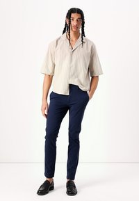 Chemise à manches courtes beige clair avec des rayures verticales, associée à un pantalon slim en bleu marine et des mocassins noirs.
