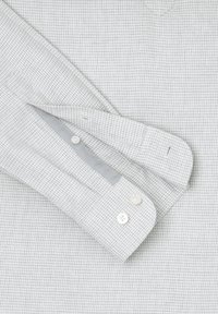 Camicia grigia chiara a quadri con polsini abbottonati, caratterizzata da una texture liscia e motivi sottili. I bottoni sono bianchi e rotondi.