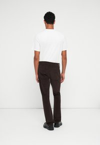 Pantalones de pana marrones con corte recto, combinados con una camiseta blanca. Presentan bolsillos traseros y una tela texturizada. Unos zapatos negros completan el look.