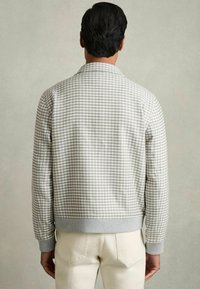 Chaqueta bomber con estampado de espiga gris, con cuello y puños acanalados, que presenta un corte relajado y una tela texturizada. Vista trasera visible.