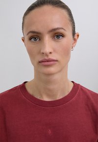 T-shirt en coton bordeaux avec un col rond, des détails cousus et un petit motif brodé sur la poitrine. Texture lisse.