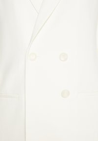 Vit dubbelknäppt blazer med slag, har två stora knappar, sidofickor och en mjuk tygstruktur.