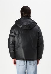 Svart pufferjacka med en glänsande yta, anpassad huva, elastiska ärmmuddar och en avslappnad passform, tillsammans med ljusblå denimjeans.