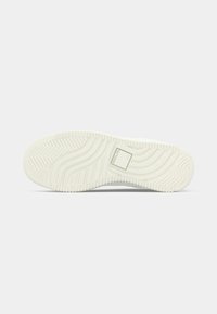 Semelle de sneaker blanche avec un motif de grip texturé et un détail de logo rectangulaire ; présente des rainures et des sillons pour traction et durabilité.