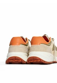 Zapatillas beige con acentos en naranja y oliva, parte superior de ante texturizado, suela de goma con la marca "HOFF" y detalle de cordones en la parte trasera.