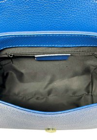 Intérieur d'un sac à main en cuir texturé bleu, avec une doublure noire, un compartiment zippé et un détail de fermeture à pression en métal.