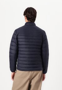 Ναυτική νεανική πικέ ζακέτα με καπιτονέ σχέδιο. Διαθέτει υψηλό λαιμό και ελαστικούς καρπούς, κατασκευασμένη από ελαφρύ, λείο ύφασμα.