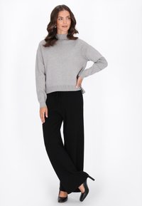 Pulover tricotat de culoare gri deschis, cu guler înalt și tiv elastic, asociat cu pantaloni negri cu picior larg și tocuri negre. Textură moale, croială lejeră.