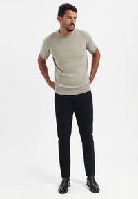 Korte mouwen rib t-shirt in lichtgrijs, gecombineerd met slim-fit zwarte broek en zwarte enkellaarsjes, tegen een neutrale achtergrond.