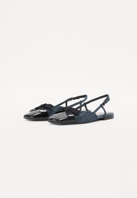 Sandales plates en denim bleu avec un capuchon de orteil noir brillant et un accent de nœud noir. Dotées d'une sangle arrière ajustable et d'un tissu texturé.