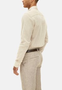 Beige linnen overhemd met lange mouwen, knoopmanchetten, subtiele textuur, gecombineerd met licht beige broek en een bruine leren riem.