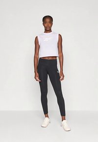 Svetlo vijoličen prilegajoč top brez rokavov z belim logotipom, kombiniran s črnimi pajkicami in lahkimi supergami. Gladek material s prilegajočim se dizajnom.