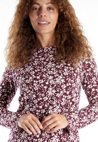 Long-sleeve top in burgundy fabric with white floral pattern, round neckline, and slightly textured finish. Features fitted sleeves.