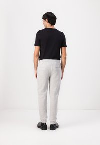 Gray sweatpants with elastic cuffs and waistband, paired with a fitted black t-shirt. Model is shown from the back. Smooth texture, casual style.