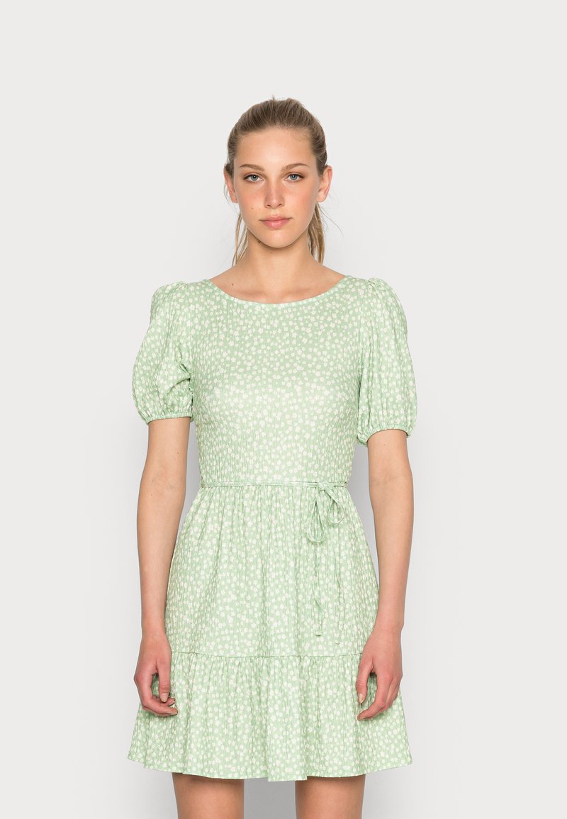 Vestido verde claro com mangas bufantes, padrão floral, cintura franzida e saia em camadas. Detalhe de laço ajustável na cintura.