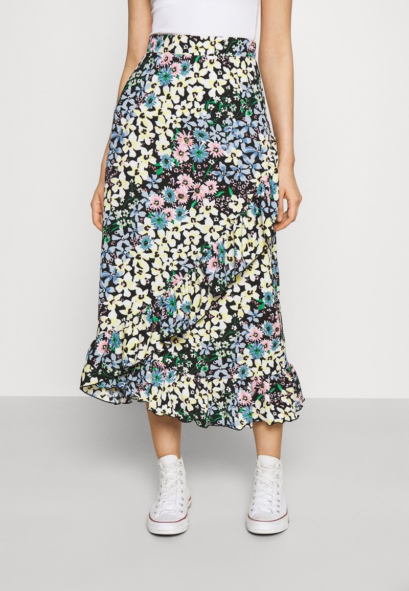 Jupe midi florale avec ourlet volanté, présentant des fleurs jaunes, bleues et roses sur fond noir, portée avec des baskets blanches et un top blanc sans manches.