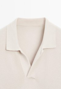 Ljust beige polo skjorta med en strukturerad stickad tyg, med klassisk krage och V-ringning för en avslappnad passform.