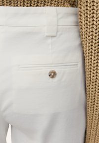 Pantalon en coton blanc avec une poche arrière dotée d'un bouton rond et décoré. Le tissu a une texture lisse et les coutures sont minimales.