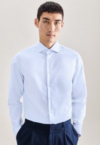 Camicia azzurro chiaro con colletto standard, maniche lunghe, patta con bottoni e bottoni bianchi a contrasto; texture liscia, vestibilità sagomata.