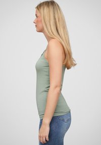 Lysegrønn tettsittende tanktopp laget av mykt stoff, med tynne stropper, kombinert med mørkeblå jeans. Toppens overflate er glatt og designet er stilrent.