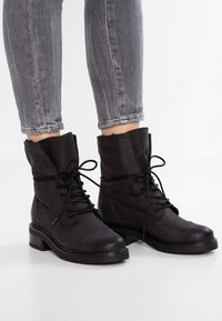 Bottes noires à la cheville en cuir lisse avec un bout arrondi, un talon plat et des lacets ; présentent des coutures discrètes et une bordure supérieure texturée.
