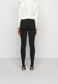 Jeans negros ajustados de cintura alta, con bolsillos traseros, combinados con un suéter de punto trenzado color crema y tacones de aguja negros.