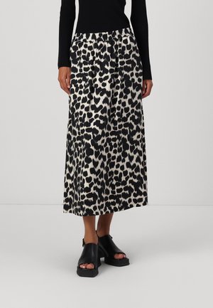 Femme portant un haut noir à manches longues, une jupe midi imprimée léopard noire et blanche, et des chaussures à plateforme noires ouvertes au bout.