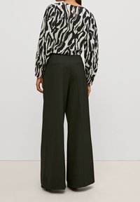 Blouse à motifs noir et blanc avec de longues manches ballon, associée à un pantalon taille haute à jambes larges de couleur vert foncé, muni de poches arrière.