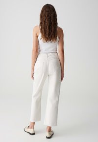 Witte high-waisted jeans met rechte pijpen, rafelrand, achterzakken en een gestructureerde afwerking, gecombineerd met beige instappers.