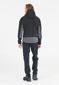 Schwarze und graue Kapuzenjacke mit elastischen Bündchen und Rückenbelüftung, kombiniert mit passenden leichten Hosen und robustem schwarzen Schuhwerk.