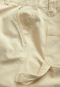 Pantalons en coton beige avec une poche avant et des passants de ceinture, dotés de coutures visibles et d'une texture lisse.