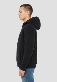 Schwarzer Baumwoll-Hoodie mit Kängurutasche, gerippten Bündchen und Saum. Verfügt über eine Kapuze mit Kordelzug und dezentes Branding am Ärmel.