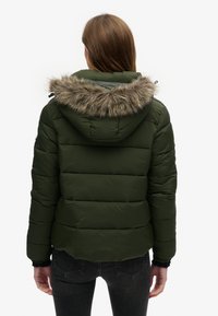 Doudoune vert olive avec une capuche à bord en fausse fourrure, design matelassé, poignets élastiques et un ourlet arrondi à l'arrière.