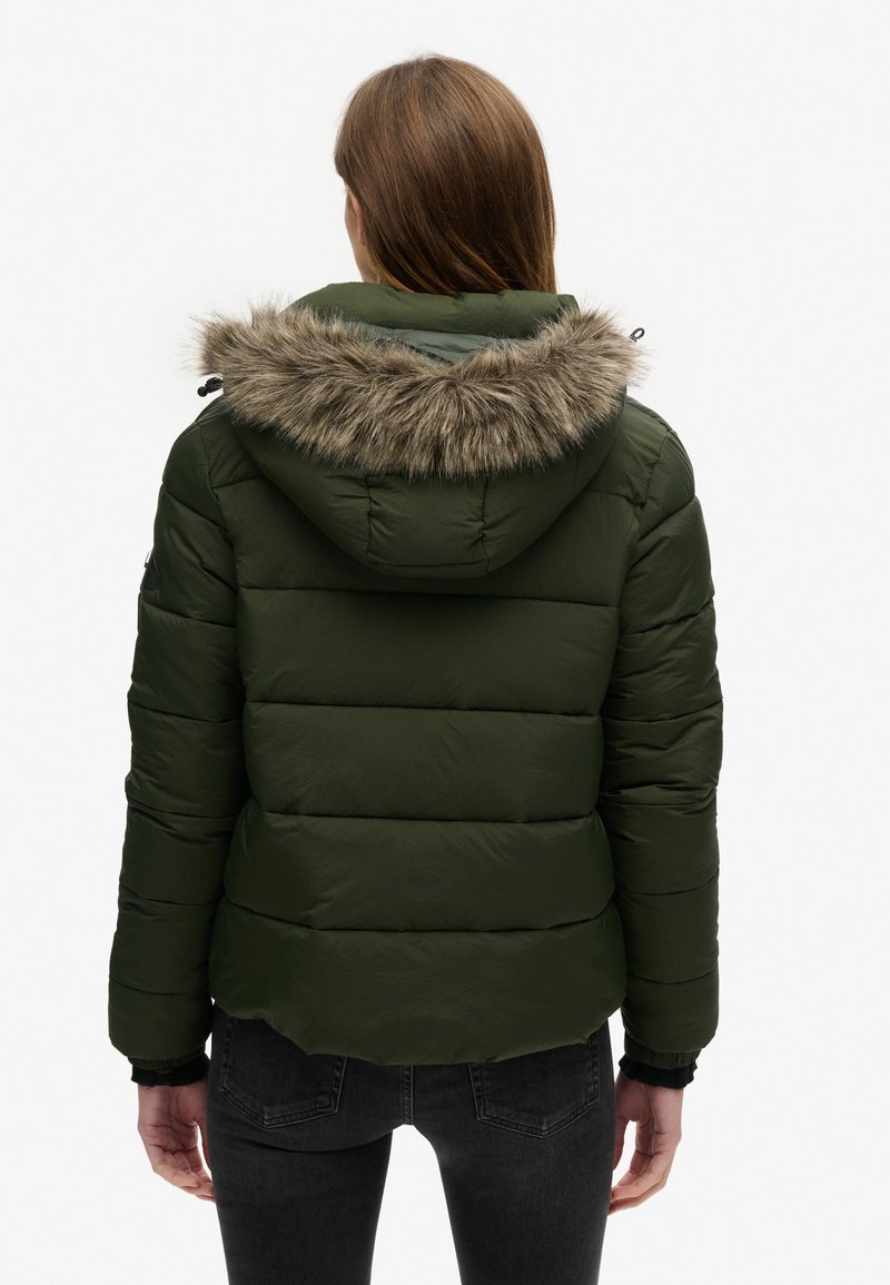 Giubbotto imbottito verde oliva con cappuccio rifinito in pelliccia sintetica, design trapuntato, polsini elasticizzati e orlo arrotondato sul retro.