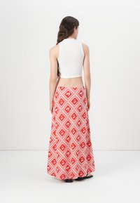 Blusa corta blanca combinada con una falda maxi roja que presenta un patrón geométrico de diamantes y acentos blancos. Sandalias planas negras completan el look.