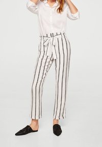 Pantaloni a righe bianche e nere con vita legata, realizzati in tessuto leggero. Abbinati a una camicia bianca con bottoni e scarpe nere slip-on.