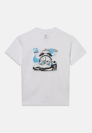 T-shirt blanc Nike avec graphique de baskets, une horloge indiquant midi, logo swoosh bleu et petite boîte à chaussures Nike bleue.