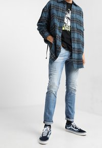 Sininen ruudullinen napillinen paita, musta graafinen t-paita sen alla, vaaleansiniset farkut ja tummansiniset lenkkarit valkoisilla yksityiskohdilla. Rentoa kerrospukeutumista.