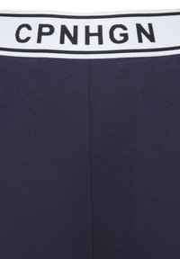 Jūras zila legingi ar melnu un baltu elastīgu jostasvietu, kurā ir teksts "CPNHGN" resnām melnām burtiem. Gluda, elastīga auduma.