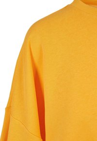 Camiseta de algodón amarilla extragrande con cuello acanalado y mangas sueltas, que muestra una textura suave y un color sólido y sencillo.